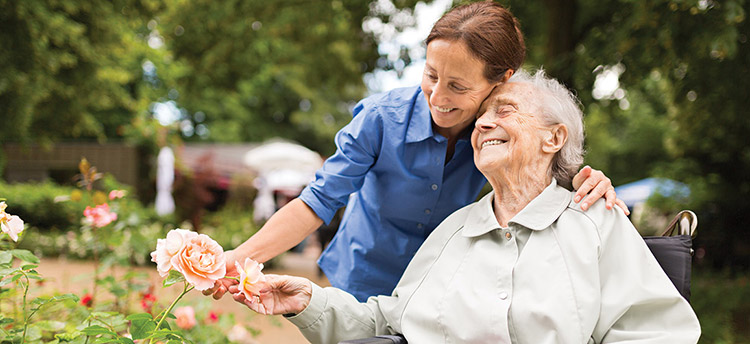 A happy senior woman and her caregiver looking at flowers